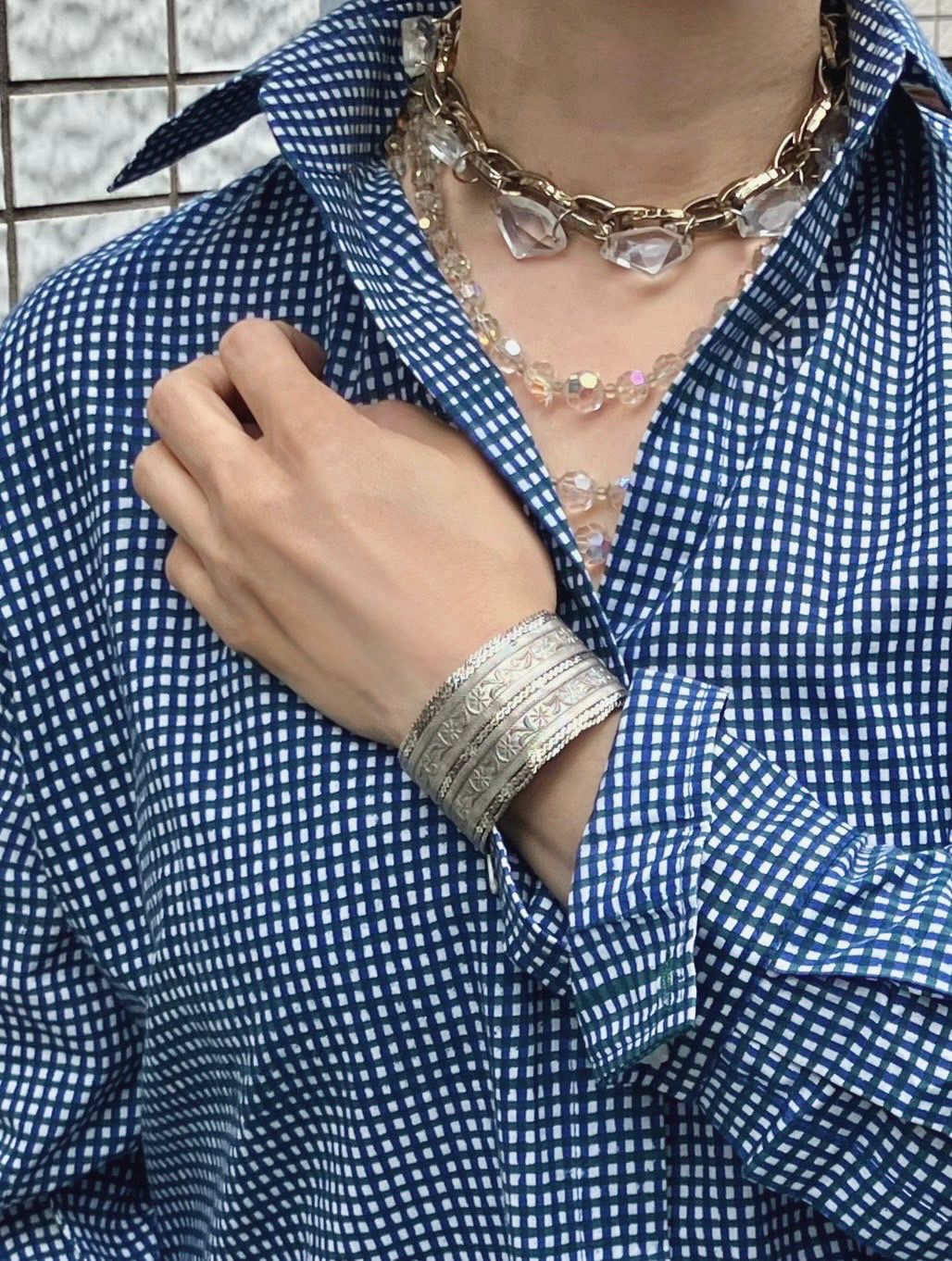 Person wearing a blue and white checkered shirt with jewelry including a necklace and bracelet.
