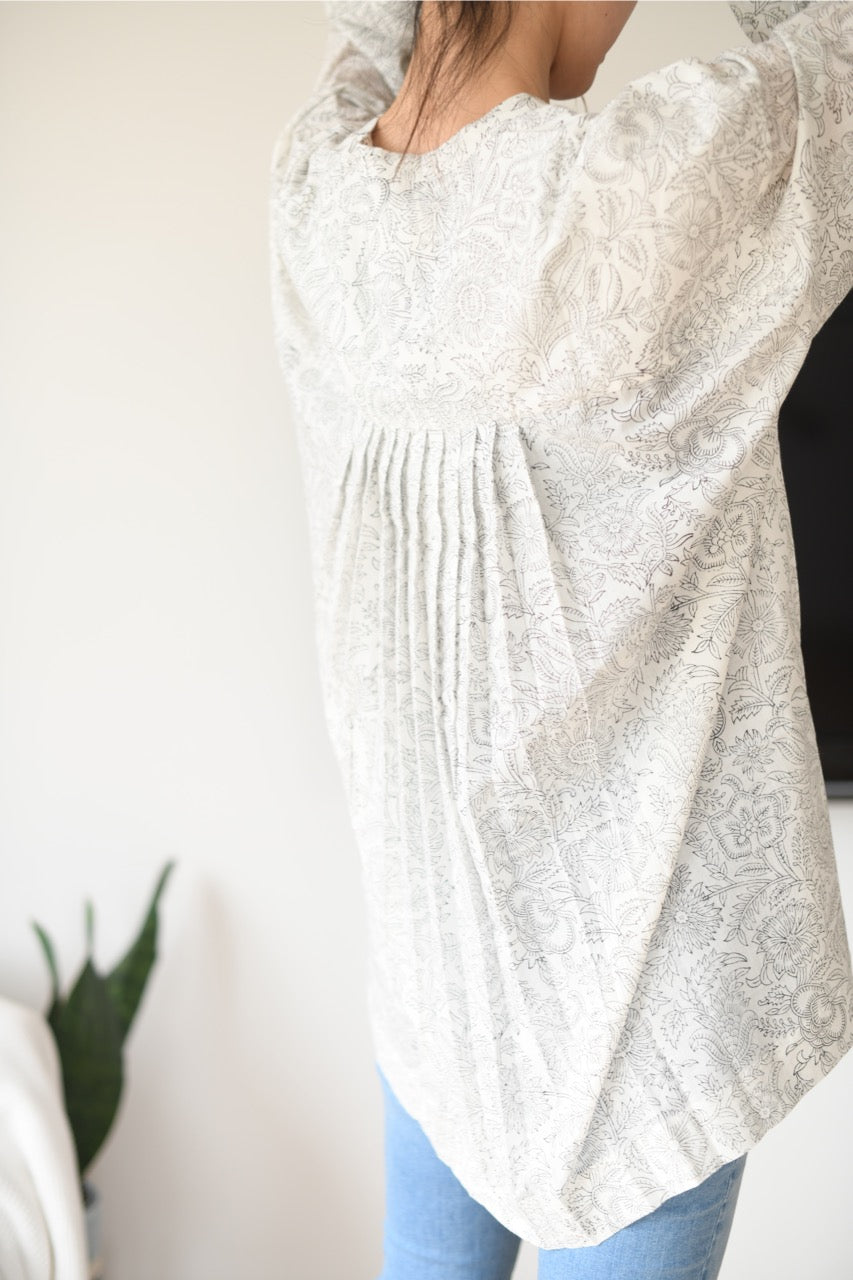 White and black printed pleated top worn by a person with a neutral background