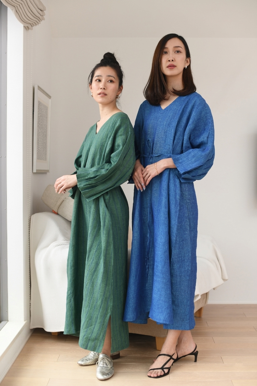 Two women standing indoors wearing green and blue linen dresses.