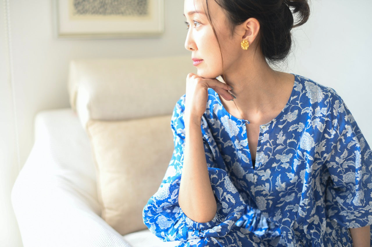 Woman in a blue floral dress sitting on a couch in a living room.