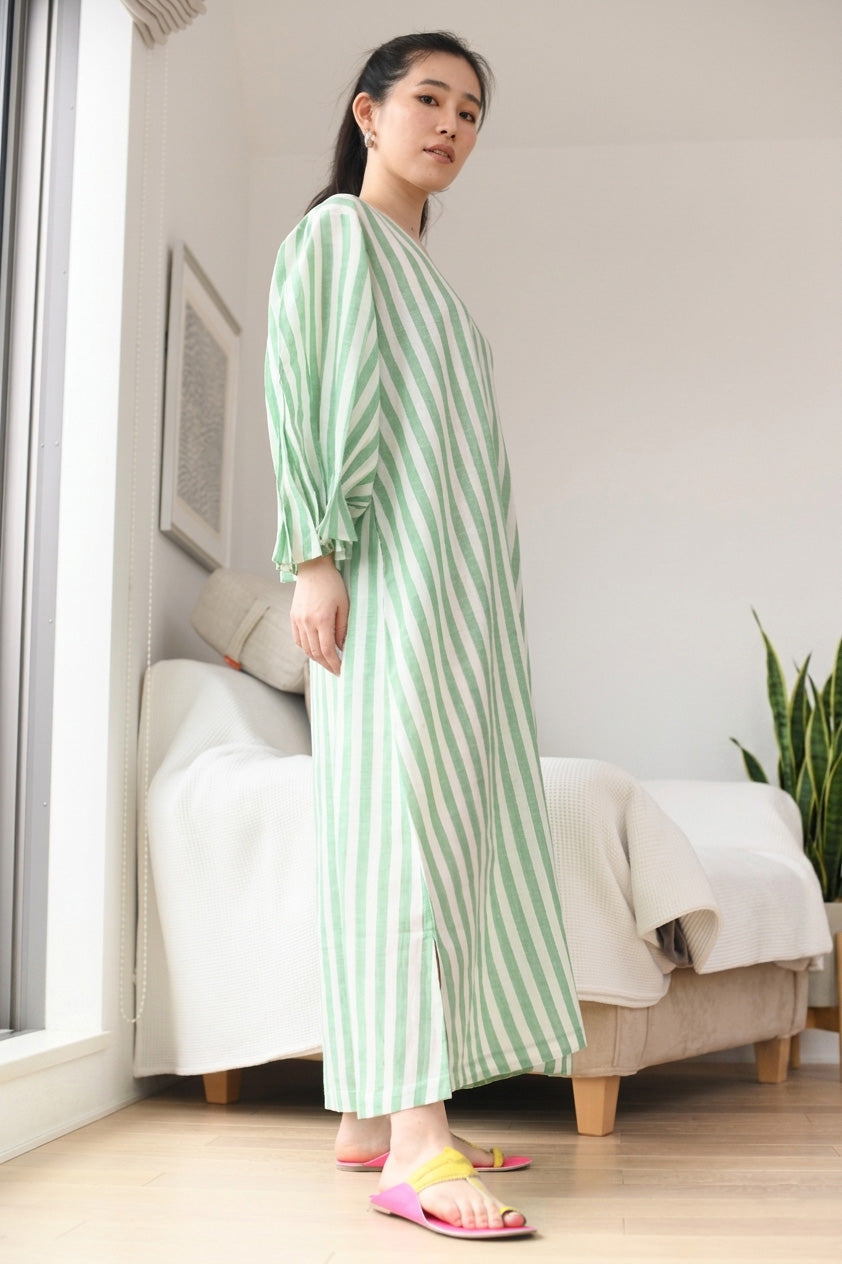 Woman wearing a green and white striped dress standing in a room with a couch and plant.