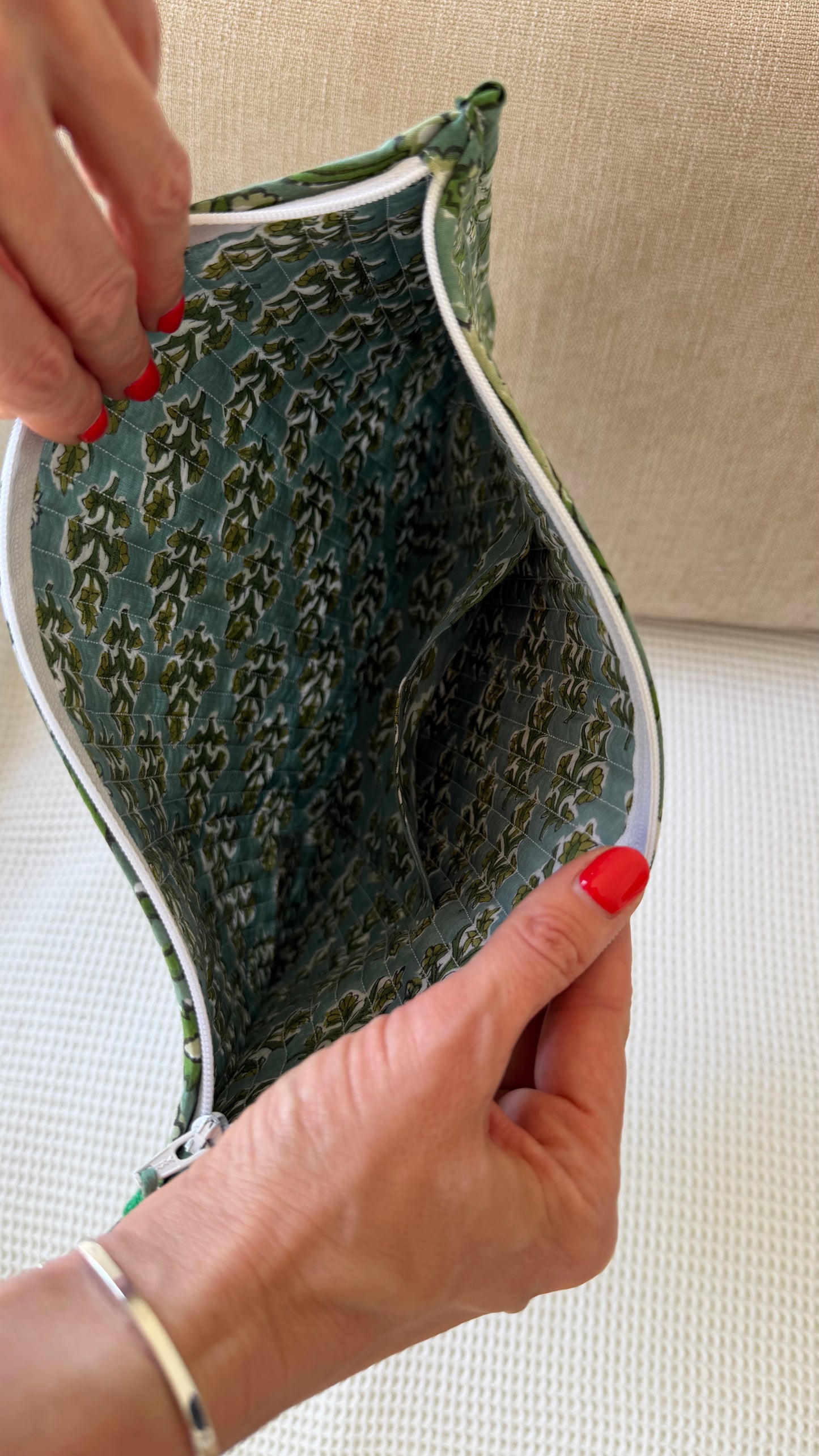 Hand holding a green patterned pouch against a beige background
