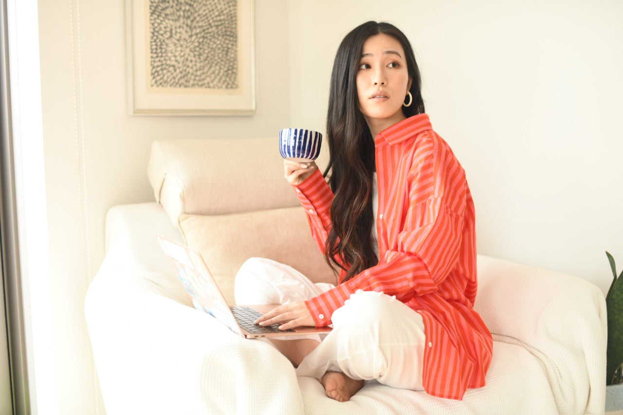Woman in a red striped shirt holding a mug and a laptop on a white couch.