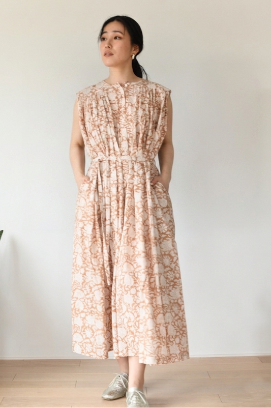 Woman wearing a floral dress standing against a plain white wall.