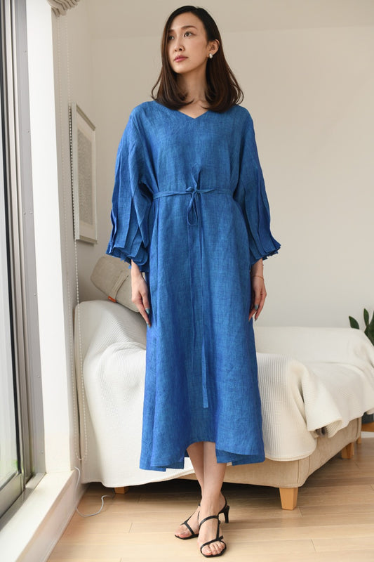 Woman wearing a blue dress standing in a room with a couch and window.