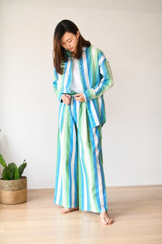Woman wearing a colorful striped outfit standing indoors with a plant in the background