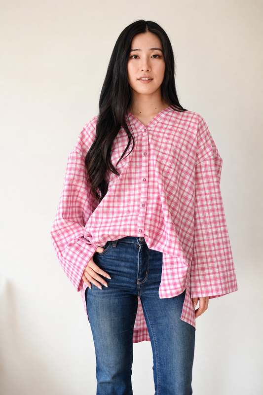 Woman wearing a pink checkered shirt and blue jeans against a plain background