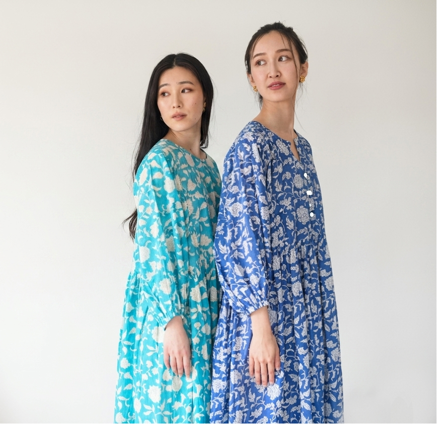 Two women wearing floral dresses standing side by side against a white background.