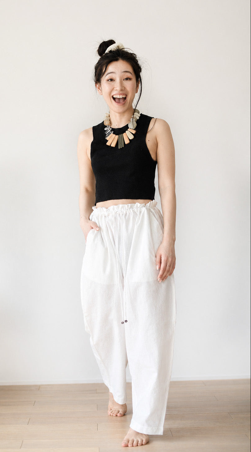 Woman wearing a black top and white pants against a plain background
