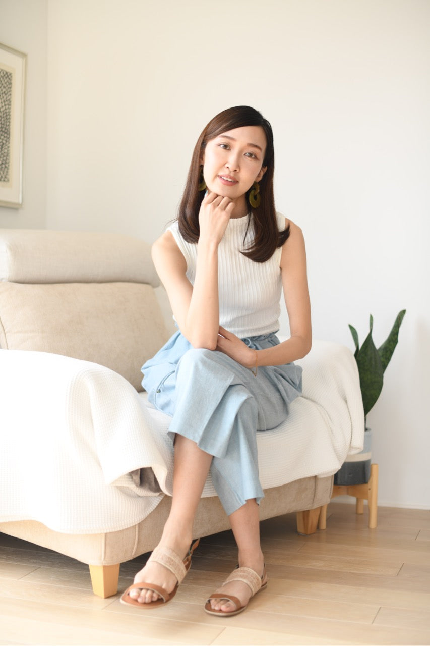 Woman sitting on a couch in a well-lit room with a plant in the background, wearing blue cotton pants.