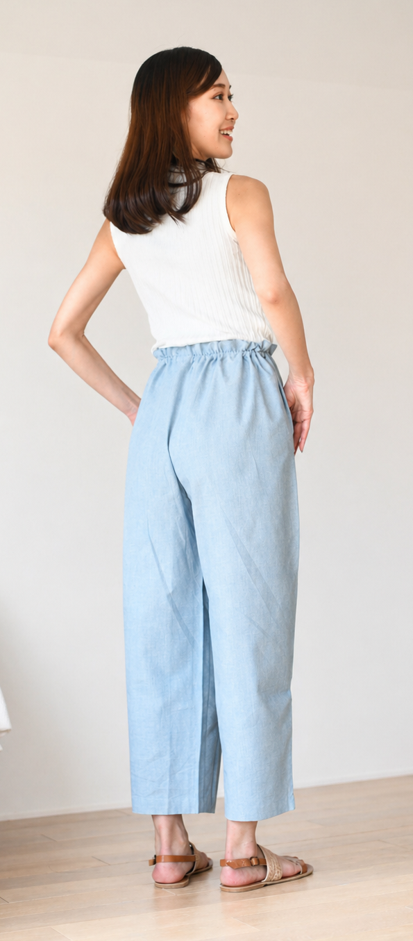 Woman wearing a white sleeveless top and light blue pants.