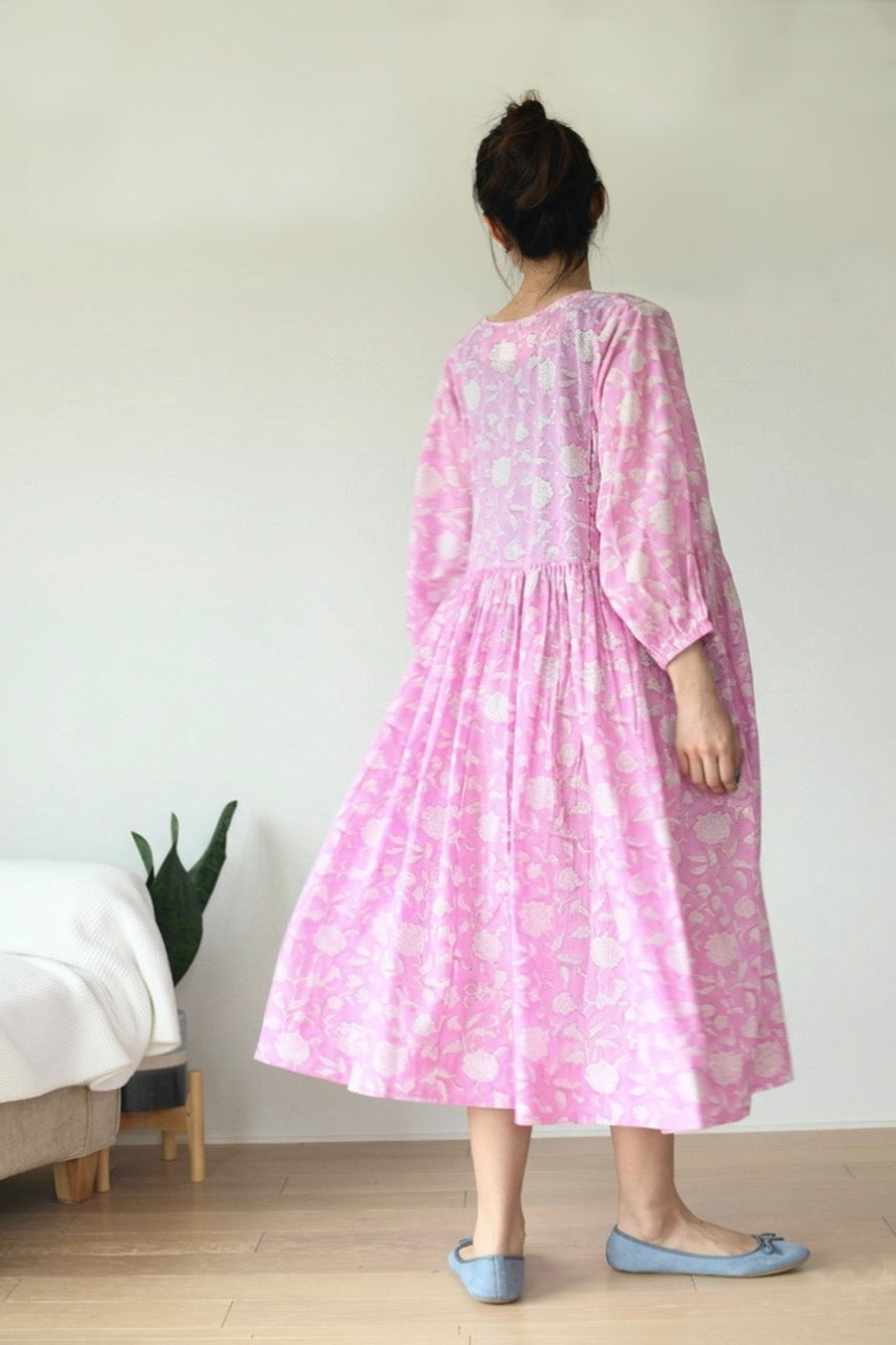 Woman wearing a pink dress with a floral pattern, standing in a minimal room.