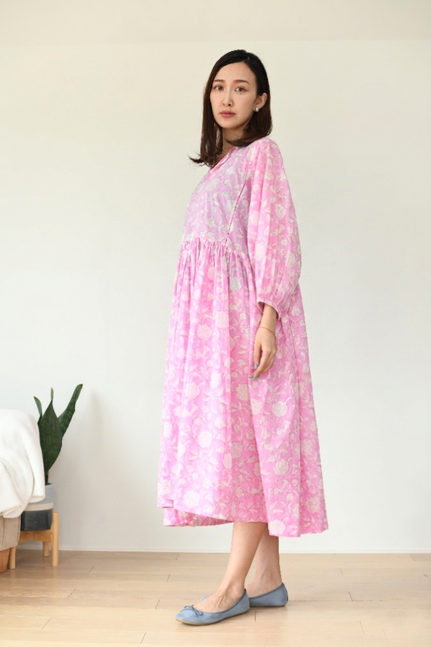 Woman wearing a pink flare dress with white floral patterns against a plain background