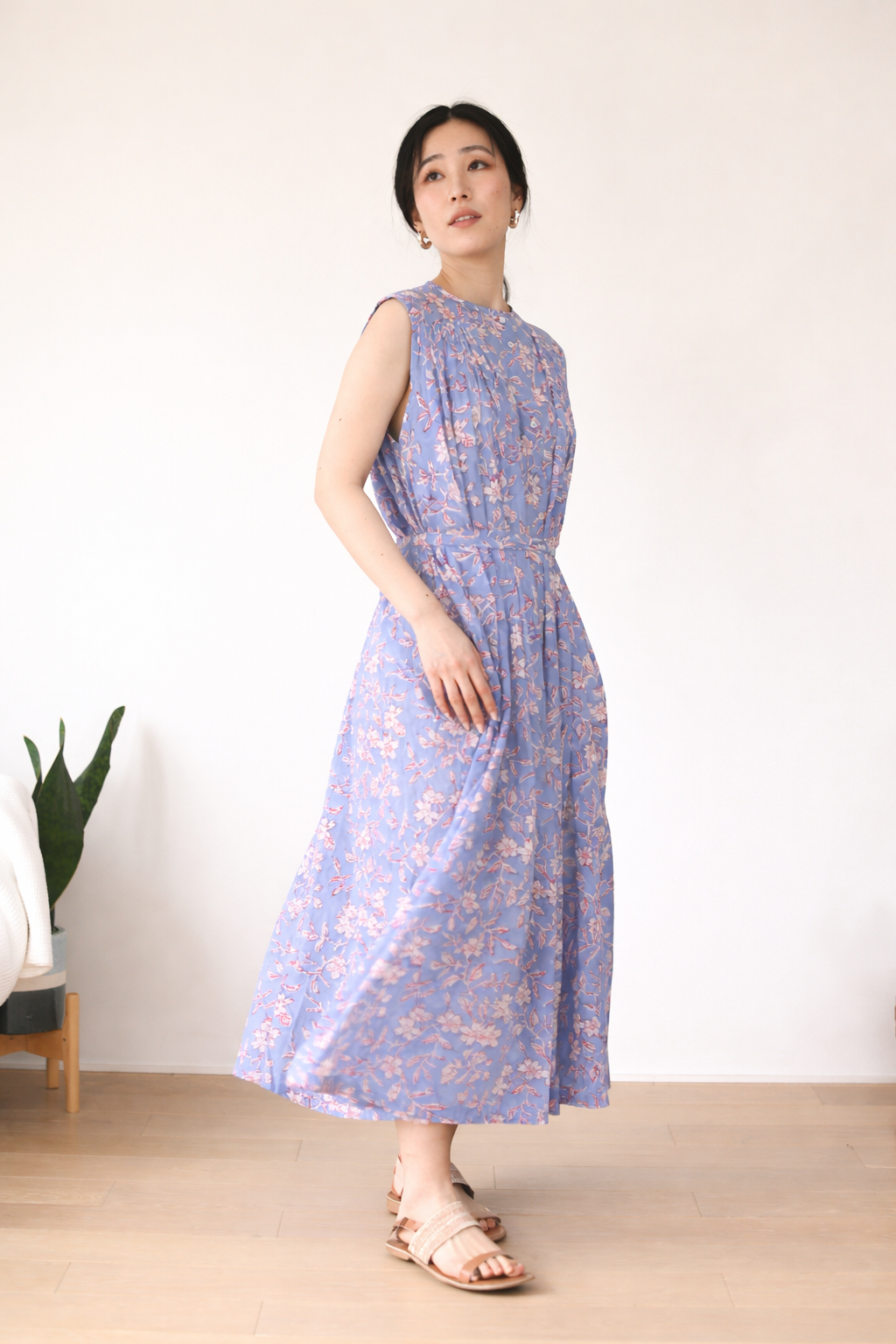 Woman wearing a blue and pink floral dress standing against a white wall.