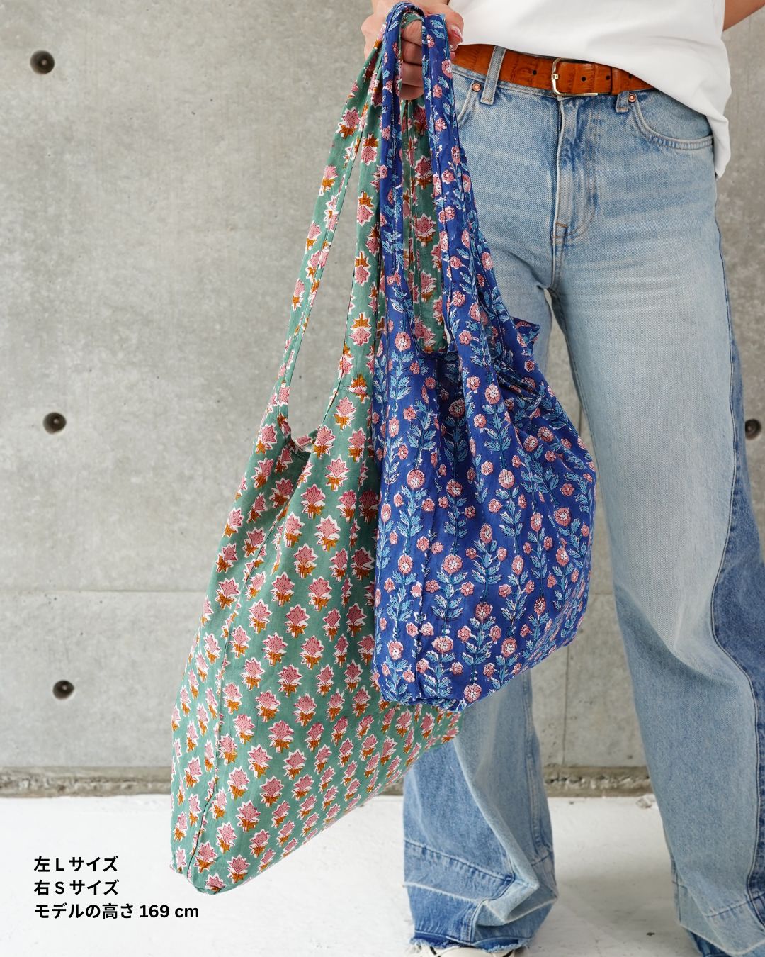 Person holding two floral-patterned cotton eco bags with a concrete wall background