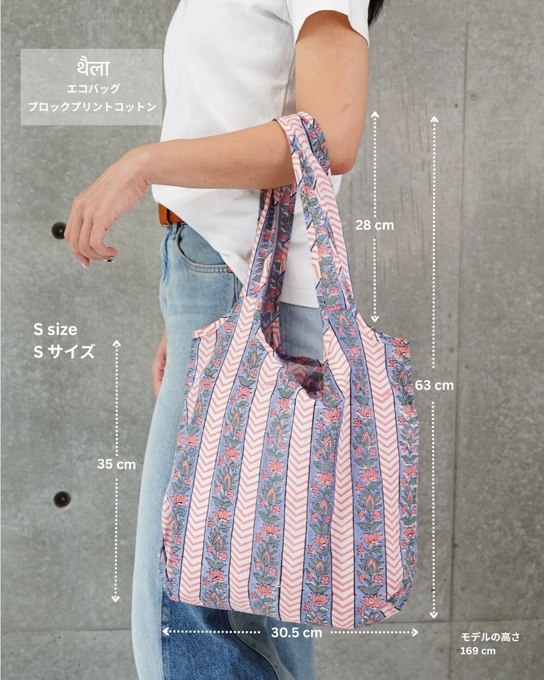 A woman holding a floral-patterned cotton eco bag with on her arm against a grey background. the measurements of the bag are also visible. 