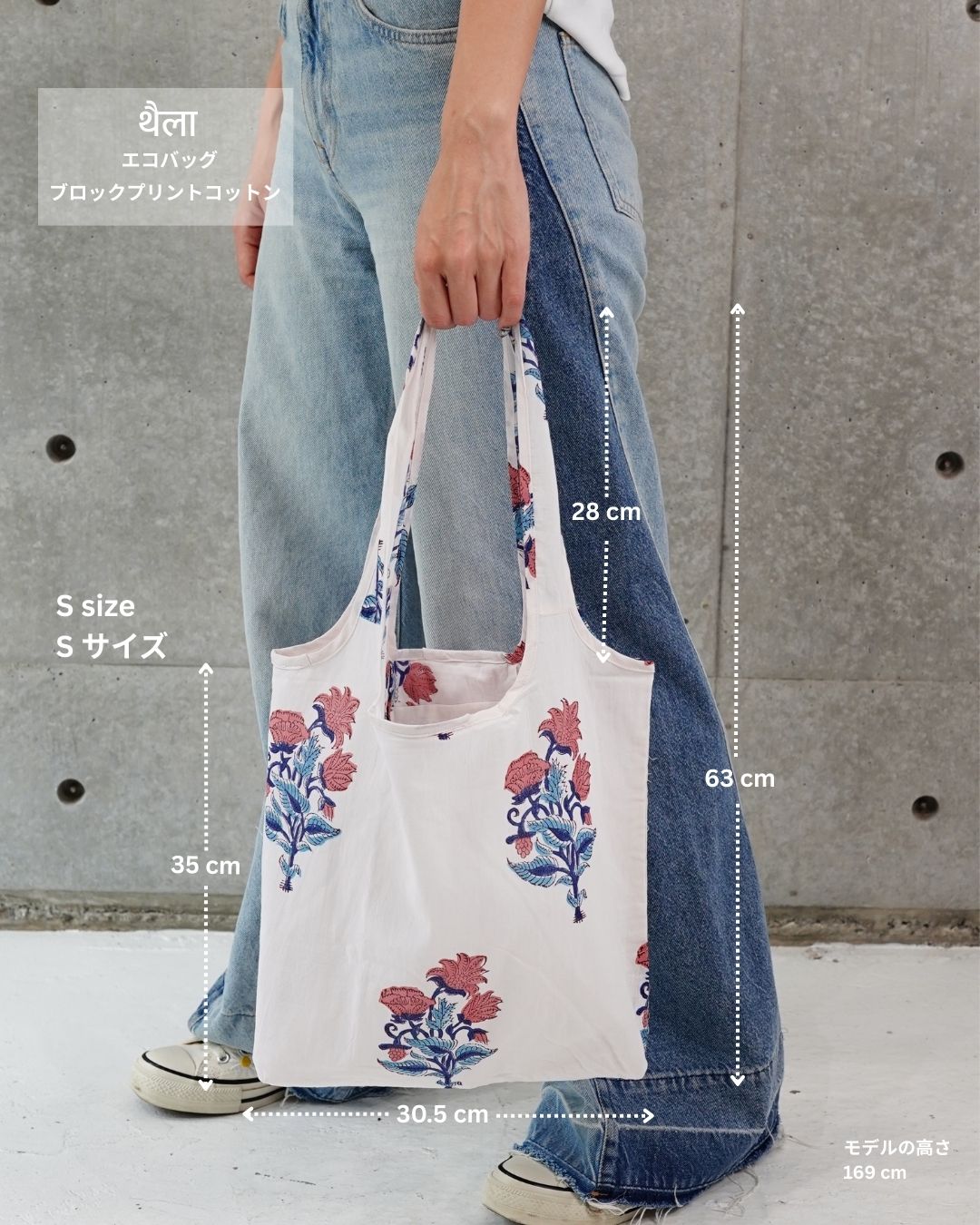 Person holding a floral tote bag with measurements against a concrete wall.