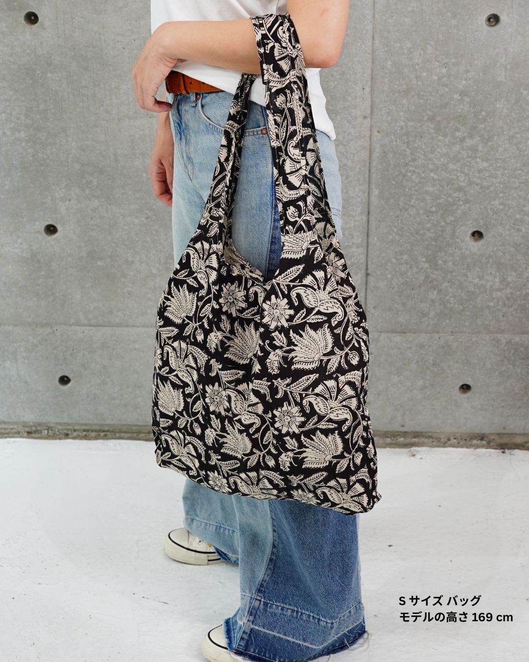 Person holding a floral-patterned bag against a concrete wall.