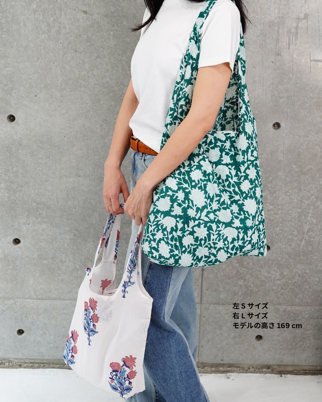 Person holding a green floral bag and a white bag with floral design against a concrete wall.