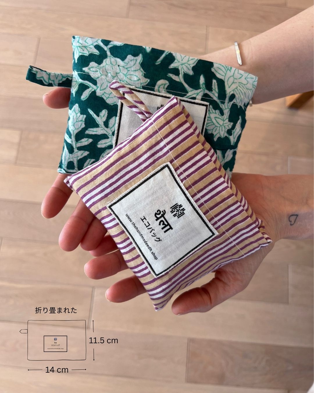 Hand holding two folded cotton eco bags, one with a striped pattern and a visible brand label, with a wooden surface in the background.