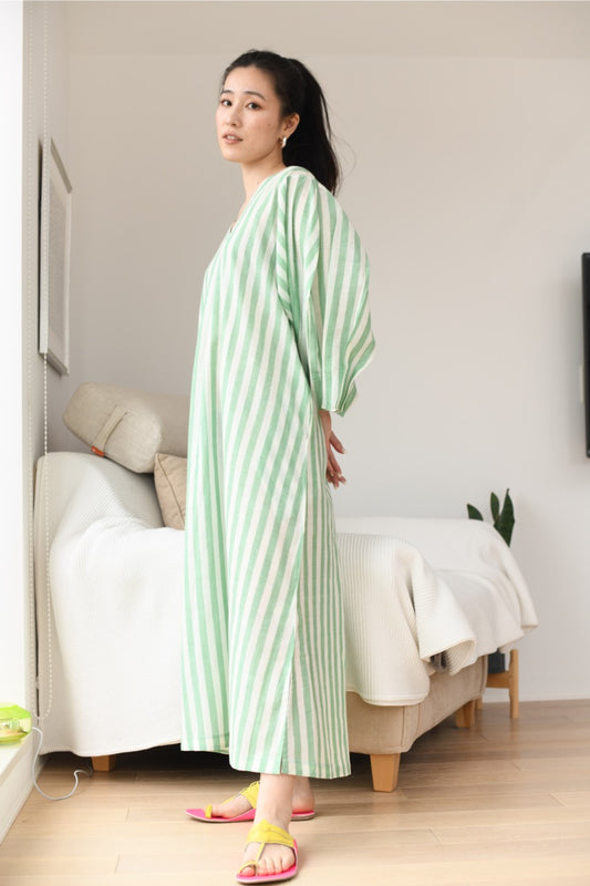 Woman wearing a green and white striped dress standing in a room with a couch.