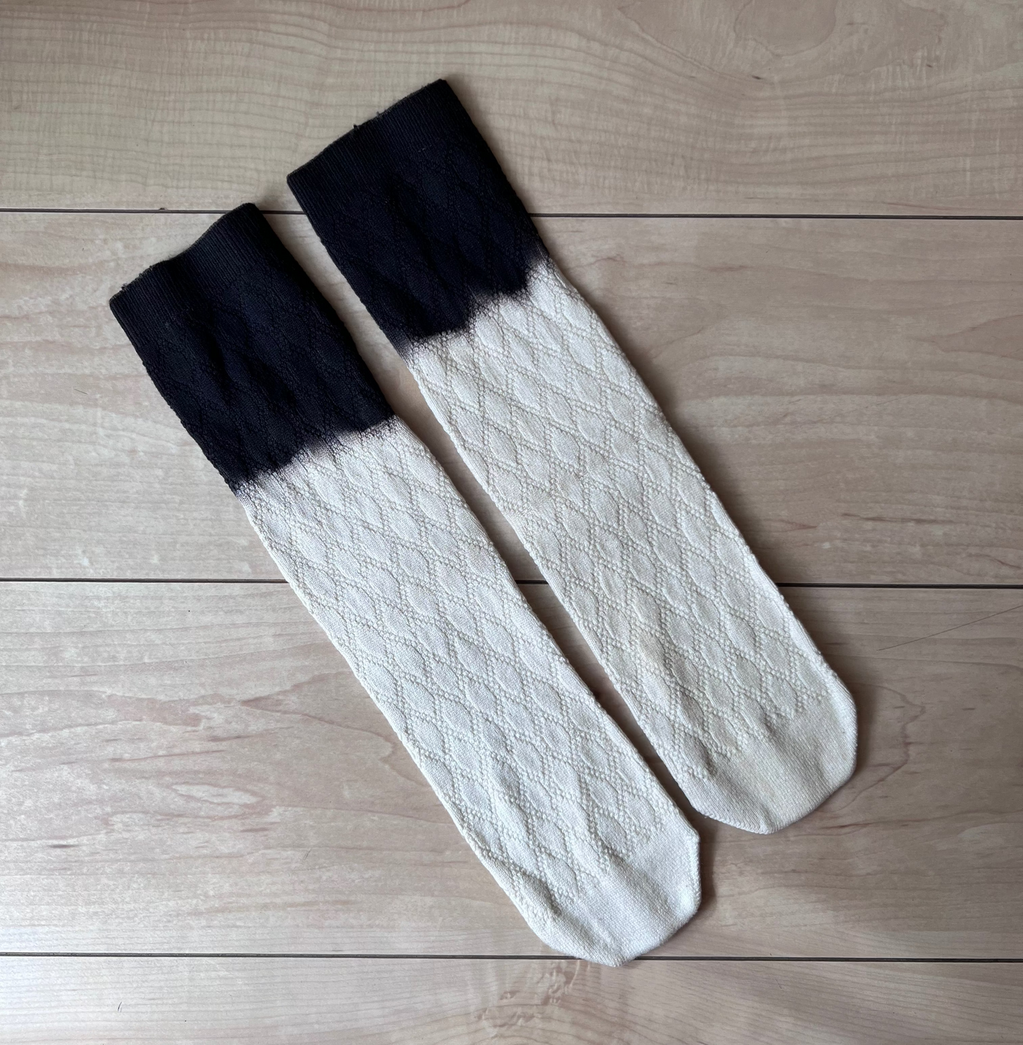 Pair of white crew socks with black natural dye cuffs on a wooden surface. 