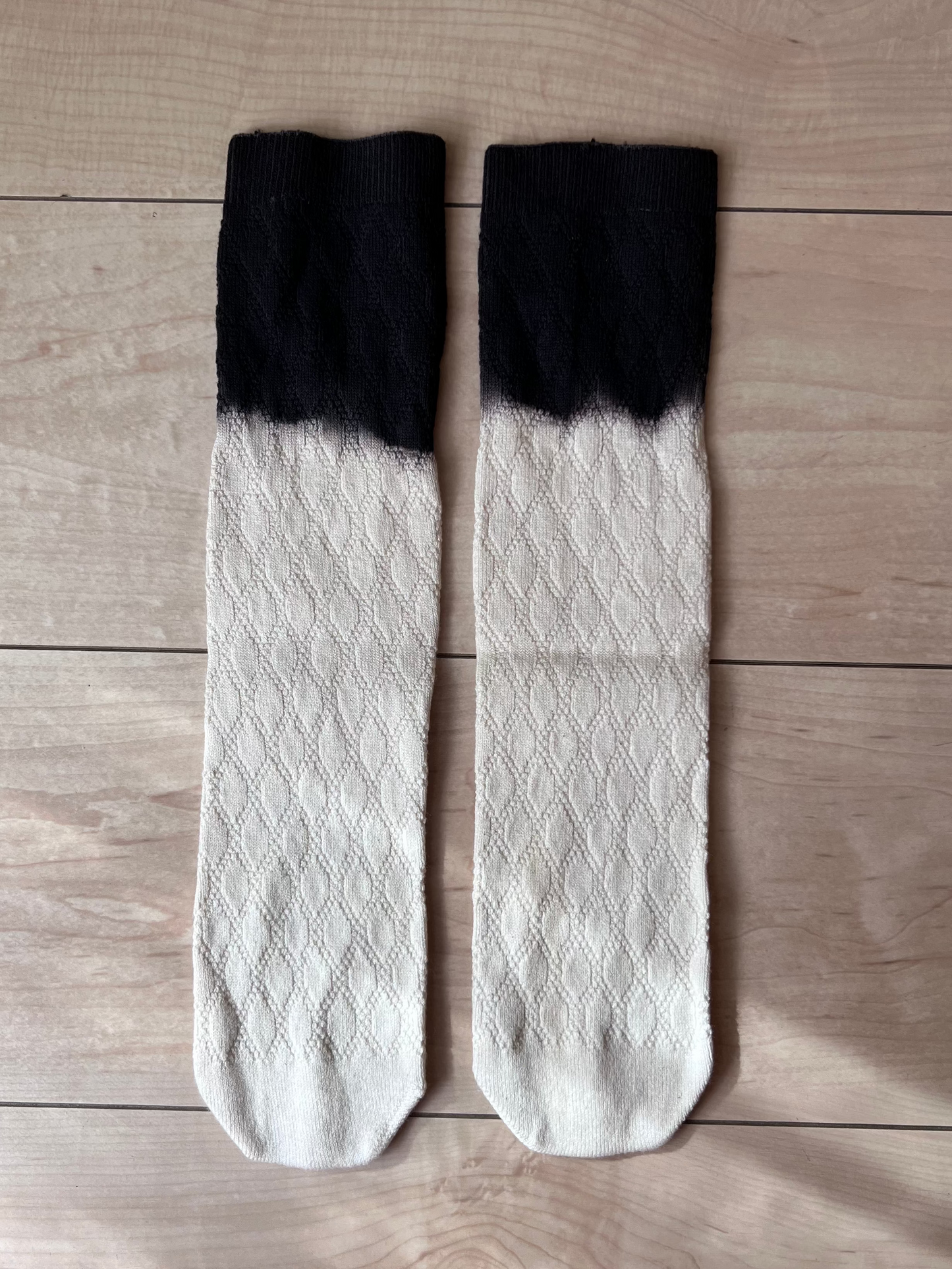 Pair of cotton socks with black tops and white bottoms on a wooden surface