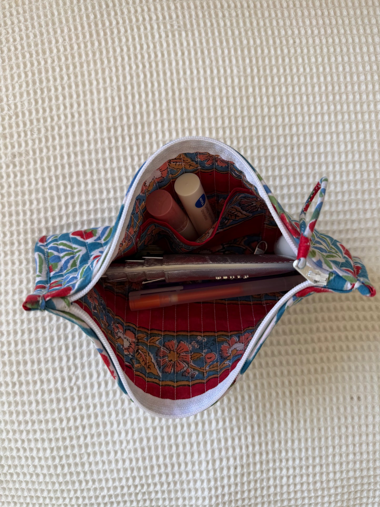 Colorful fabric pouch with stationery items on a textured beige surface