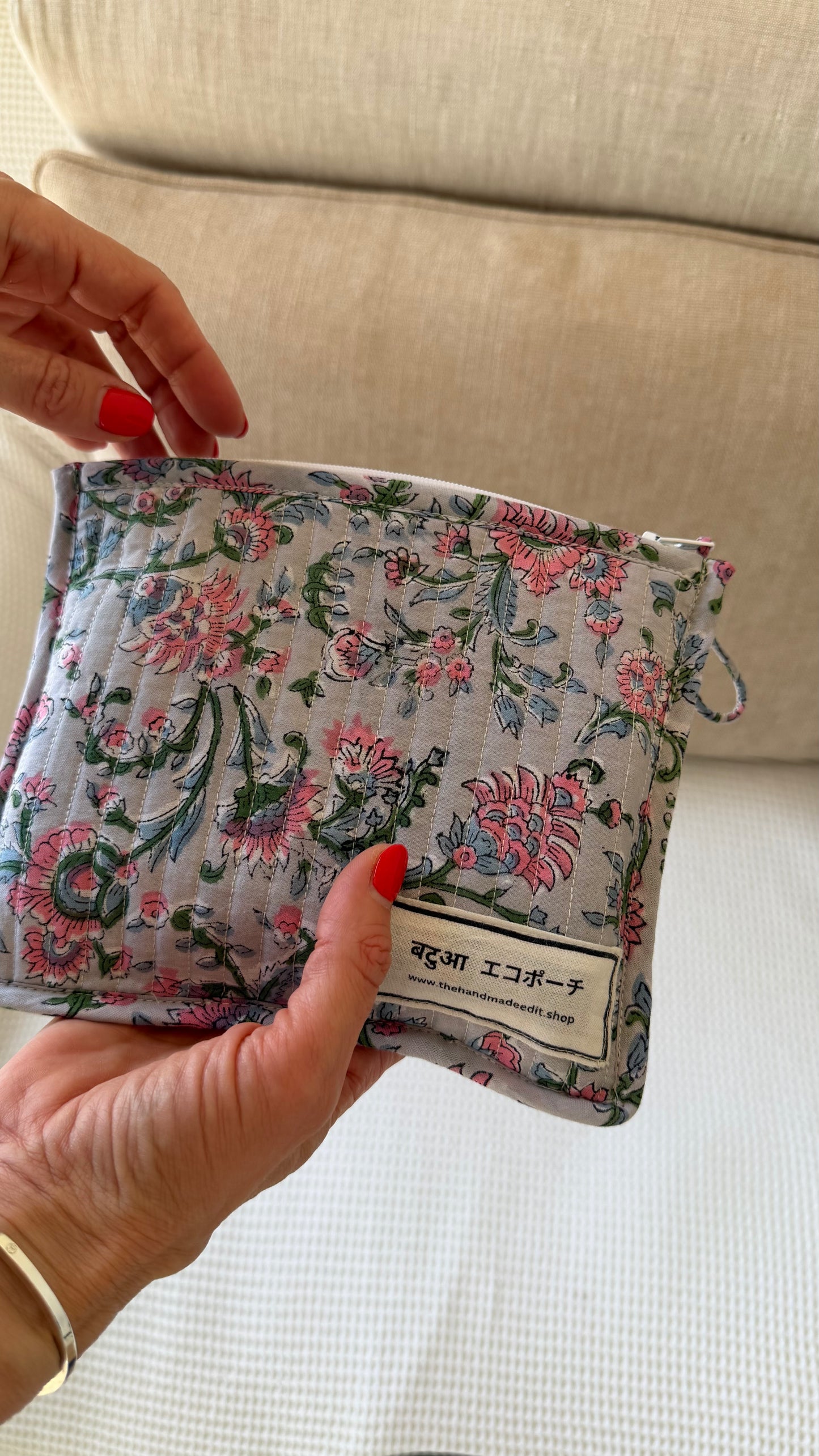 Floral-patterned fabric pouch held by a person with a beige couch in the background