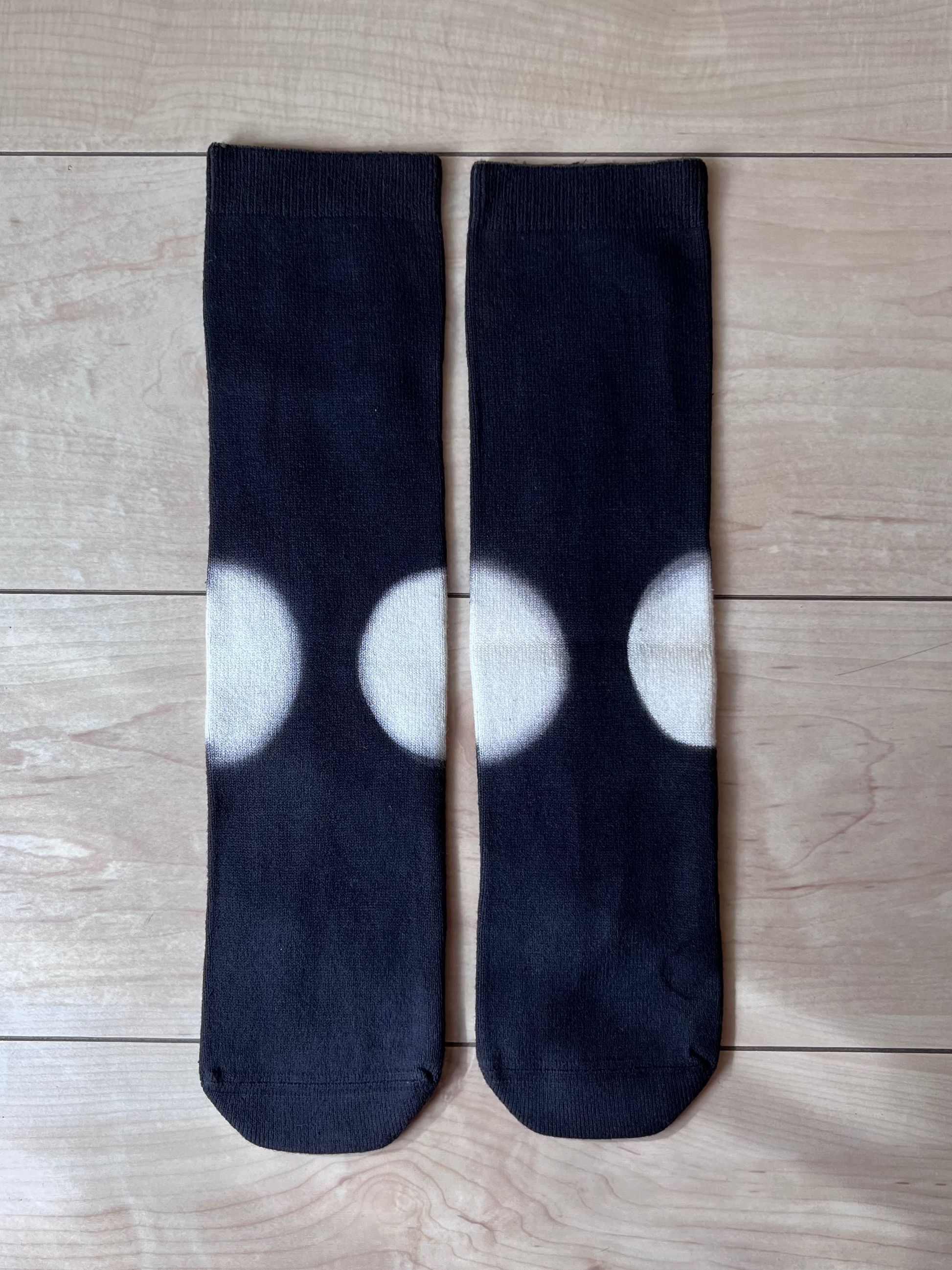 Black natural dye cotton socks with white clamp dye circle pattern on a wooden floor