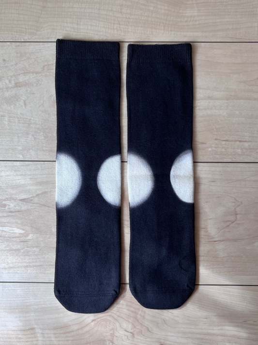 Black natural dye cotton socks with white clamp dye circle pattern on a wooden floor