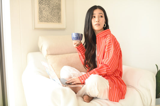 Woman in a red striped shirt holding a mug and a laptop on a white couch.
