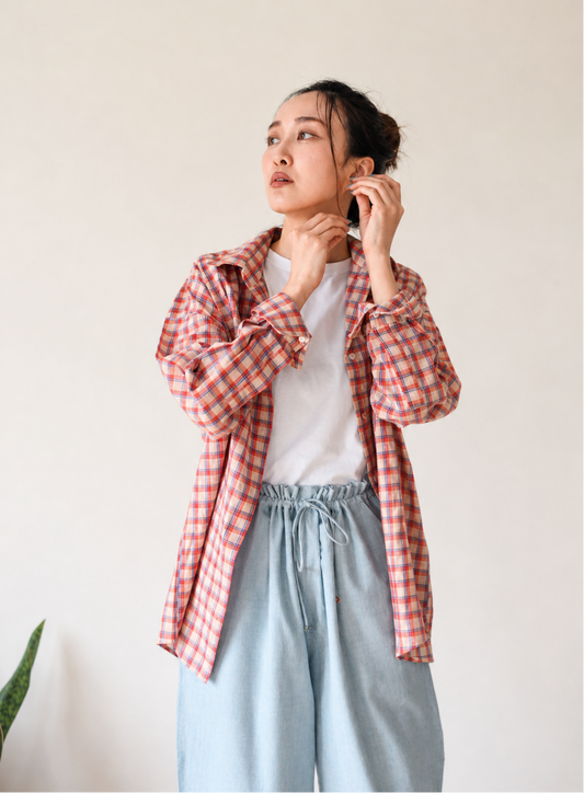 Woman wearing a red and white checkered shirt over a white t-shirt with light blue drawstring pants against a plain background