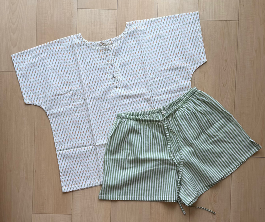 White top with peach dots and green striped shorts on a wooden floor.