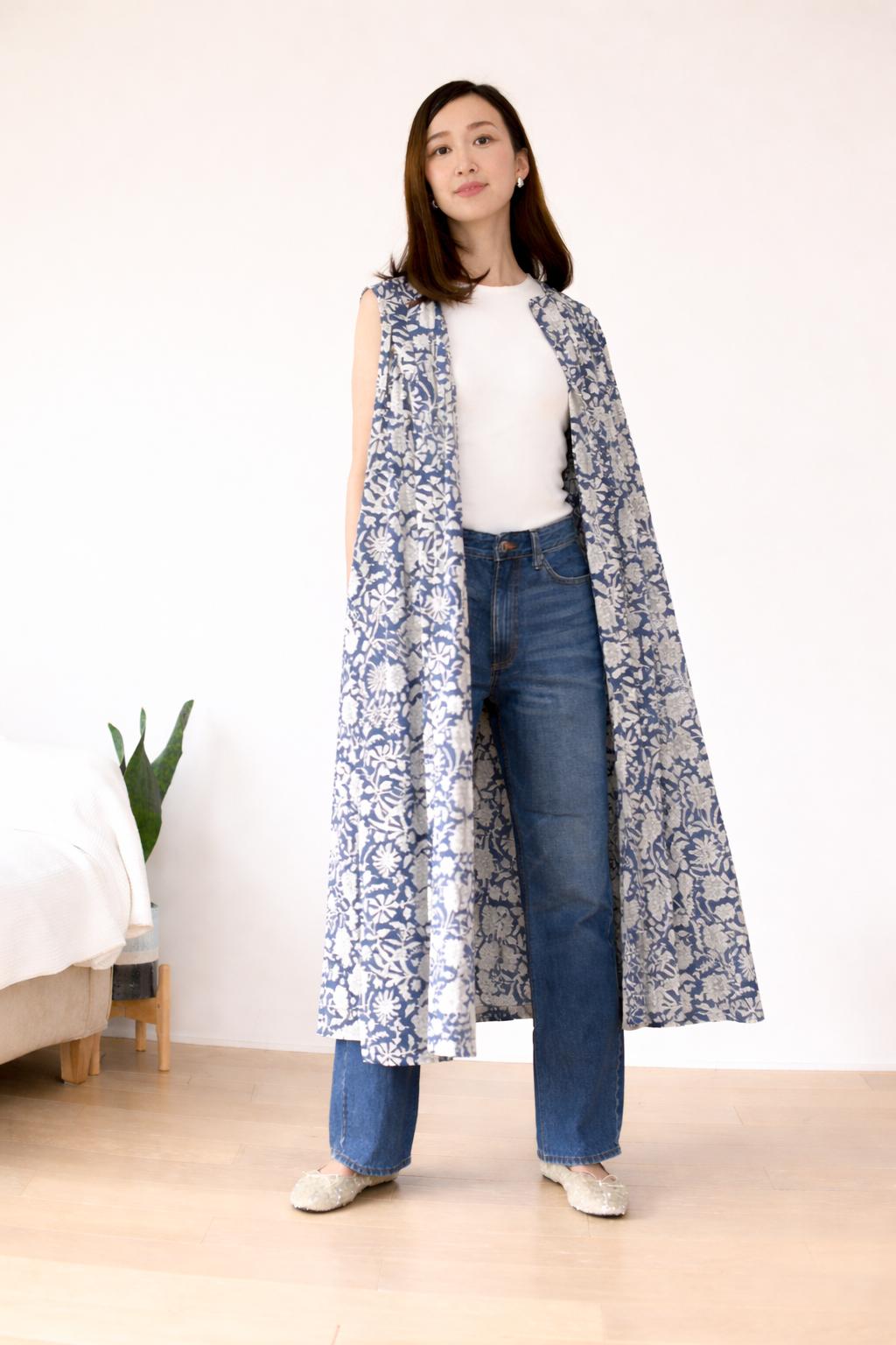 Woman wearing a long button front  floral dress over a white top and blue jeans in a minimal indoor setting.