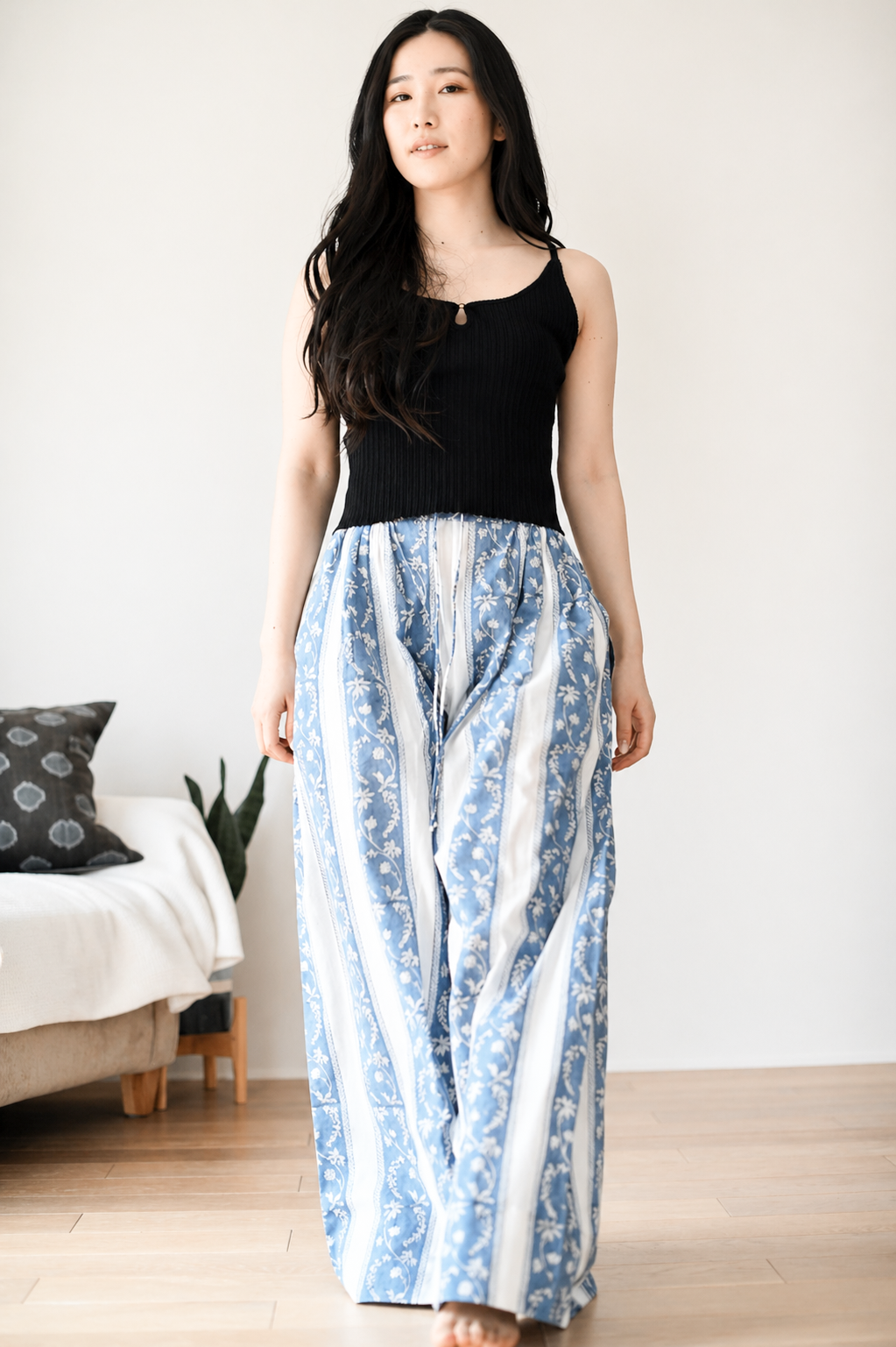 Woman wearing a black top and blue patterned pants in a room .