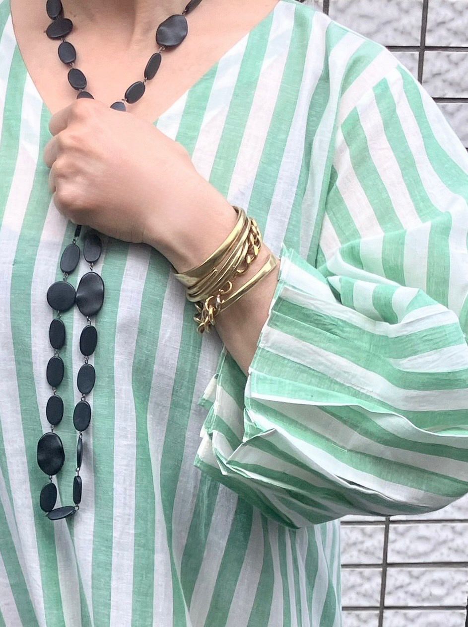 Person wearing a green and white striped garment with a gold bracelet and black necklace.