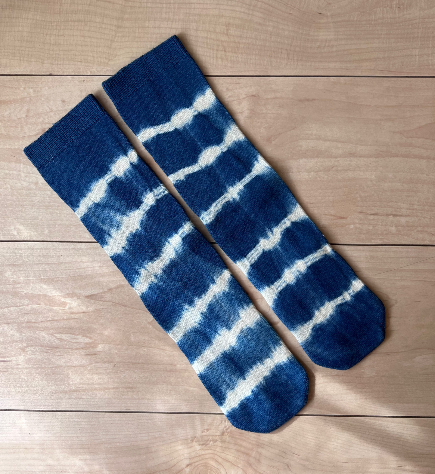 Blue and white patterned socks on a wooden surface. the socks are made of recycled cotton and dyed in shibori technique using natural indigo