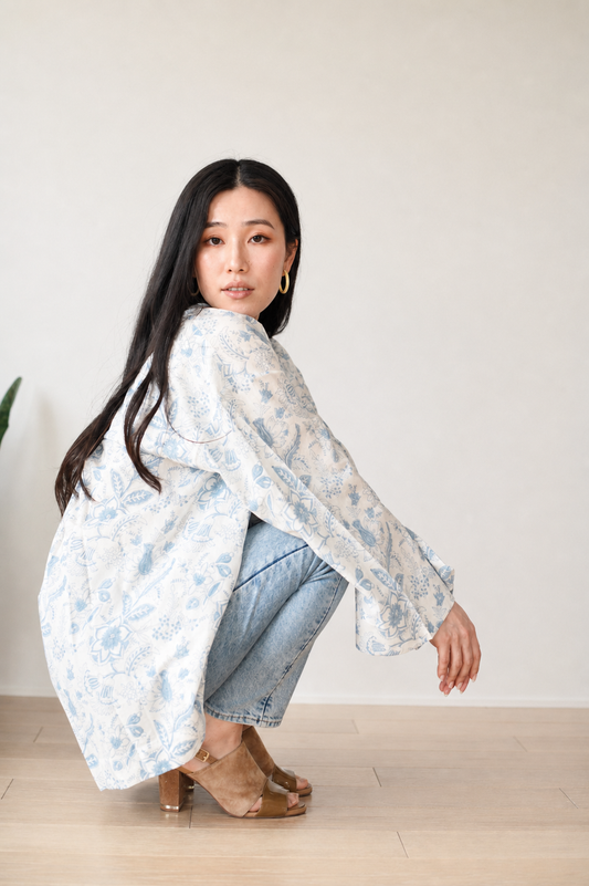 Woman wearing a light-colored floral blouse and jeans against a plain background
