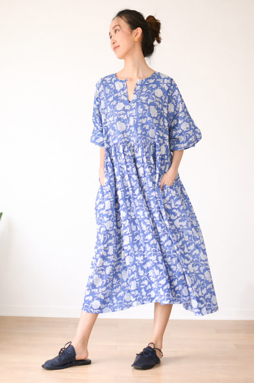Woman wearing a blue floral dress standing in a minimal indoor setting.