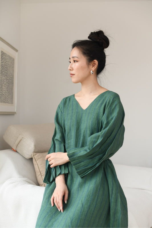 Woman wearing a green linen dress sitting on a couch in a living room.