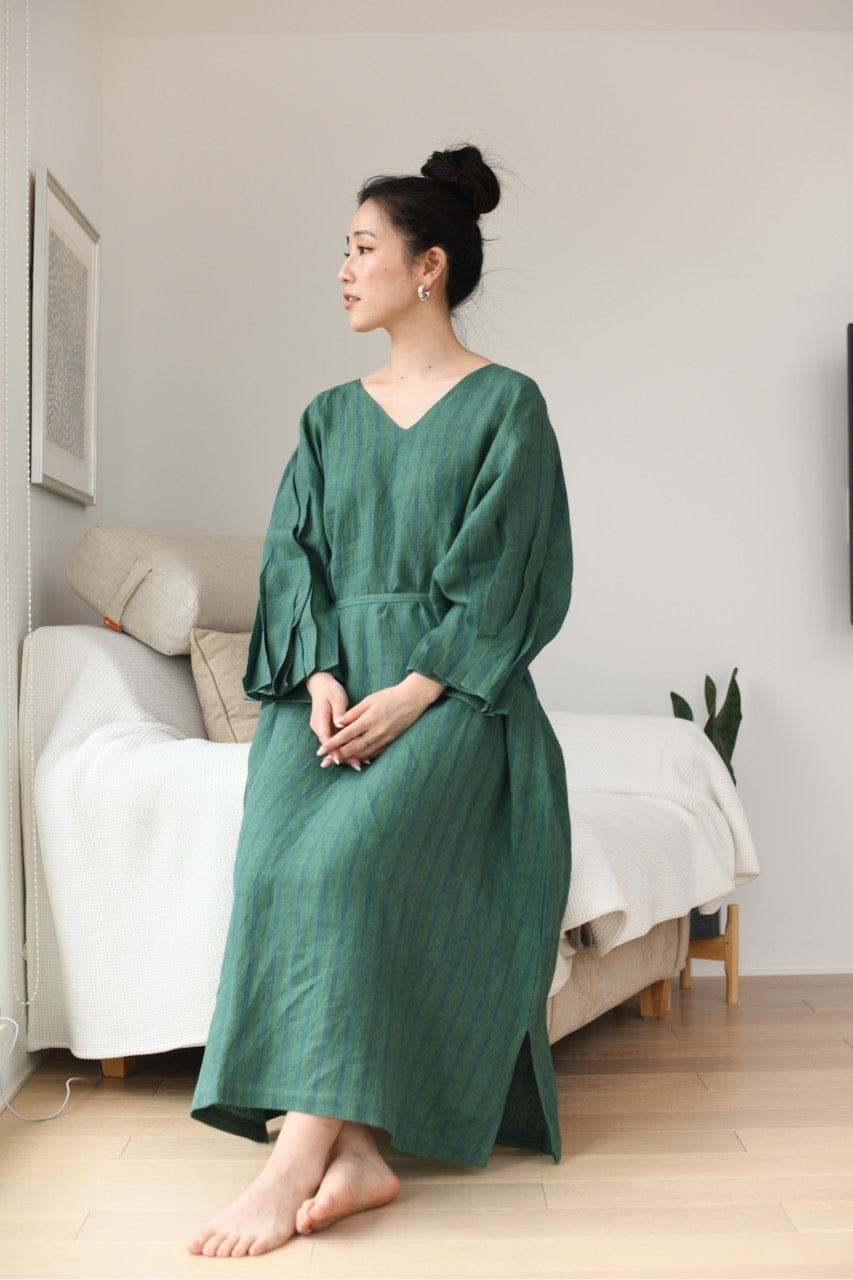 Woman in a green linen dress sitting in a room with a couch and white walls.