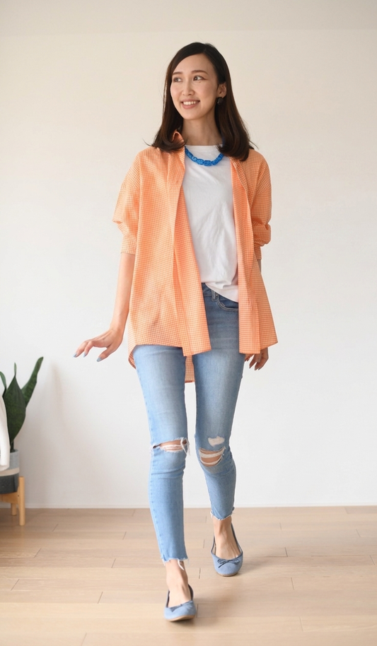 Woman wearing a peach shirt, white T-shirt, and light blue jeans indoors.