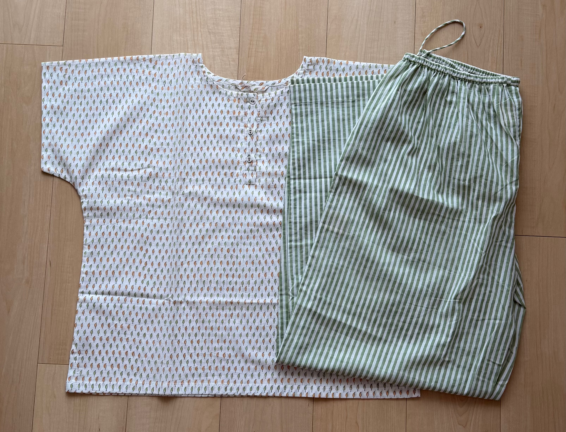White patterned top and green striped  pants on a wooden floor