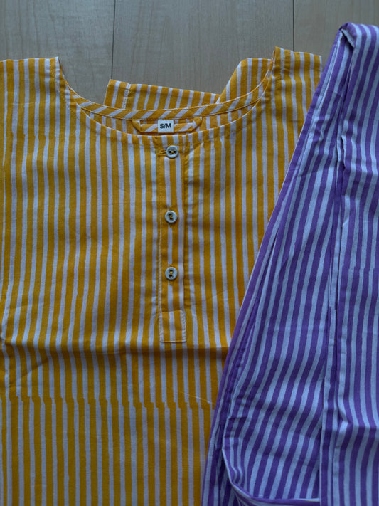 Yellow and white striped shirt with buttons next to purple and white striped pants on a wooden surface.